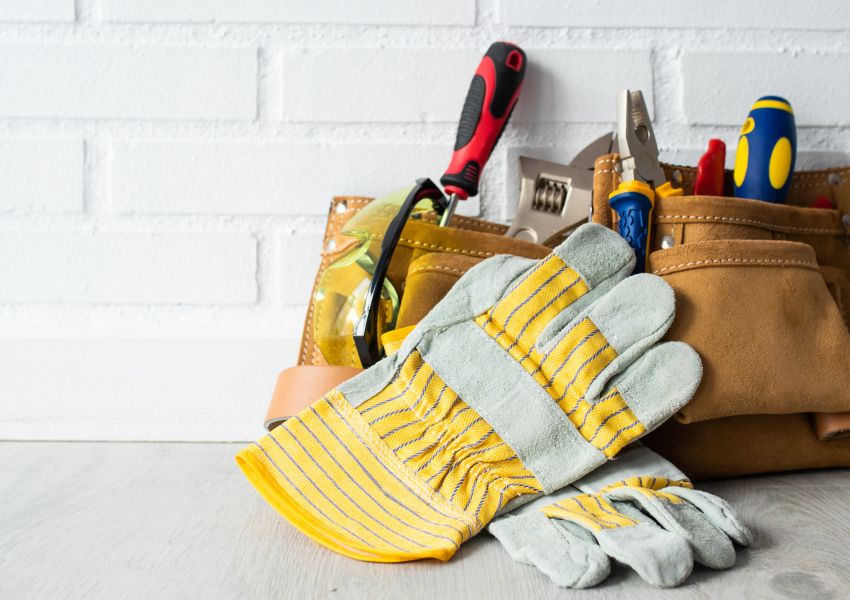 A tool box sits behind a pair of construction gloves against a white brick wall.