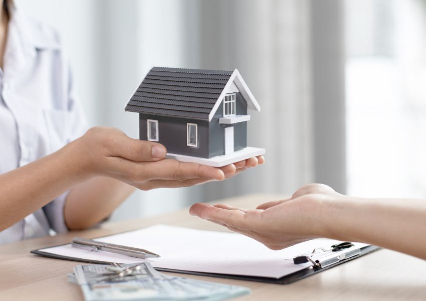 person-handing-wooden-house-to-another